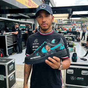 Person holding a black and blue sneaker with Mercedes-Benz and Petronas logos in a Formula 1 garage.